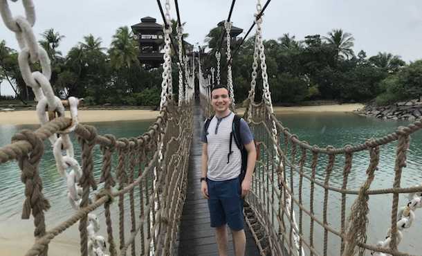Matthew Aronson on a rope bridge in Singapore near a beach